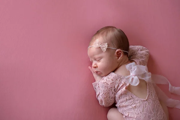 一个美丽的 沉睡的 新生的女婴身穿粉红色 花边爬衣和花边头饰 拍摄在工作室与粉红色的背景 — 图库照片