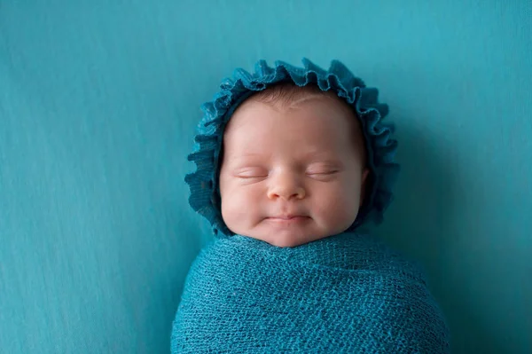 一个微笑 三周大 新生的婴儿女孩戴着帽子 捆绑在一个蓝绿色襁褓 — 图库照片