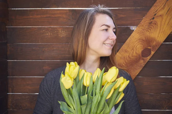 Женщина стоит у деревянной стены и держит тюльпаны — стоковое фото