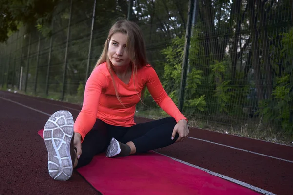 Mulher desportiva é esticado sentado em um tapete — Fotografia de Stock