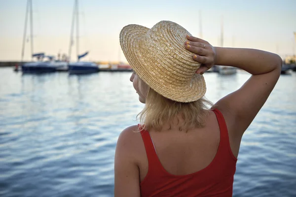 Mujer con sombrero de mimbre se sienta en el mar al atardecer — Foto de Stock