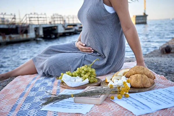 Egy terhes nő a tengerparton tartja a hasát. Piknik — Stock Fotó