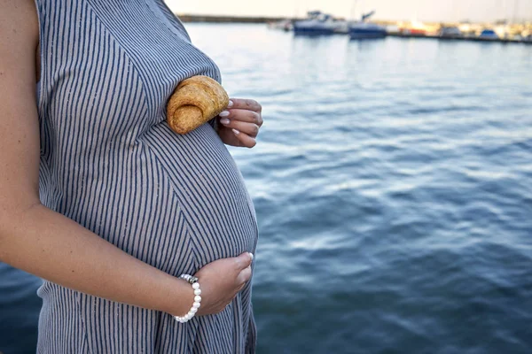 Těhotná žena drží croissant na břiše proti backgr — Stock fotografie