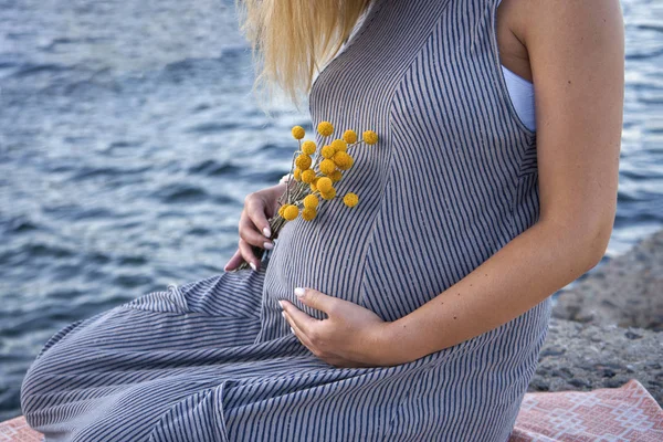 Hamile kadın göbeğini deniz kenarında tutuyor. — Stok fotoğraf