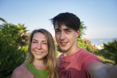 Kadın ve erkek, palmiye ağaçlarının arka planında selfie çekiyorlar.