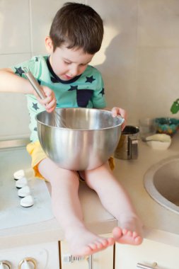 Küçük çocuk elmalı turta yapıyor. Mutfak gereçleri ve elmalı turta malzemeleri olan çocuk masaya oturur.