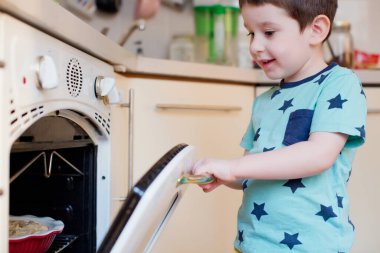 Küçük çocuk fırının yanında elmalı turta bekliyor. Küçük çocuk mutfakta pasta bekliyor.