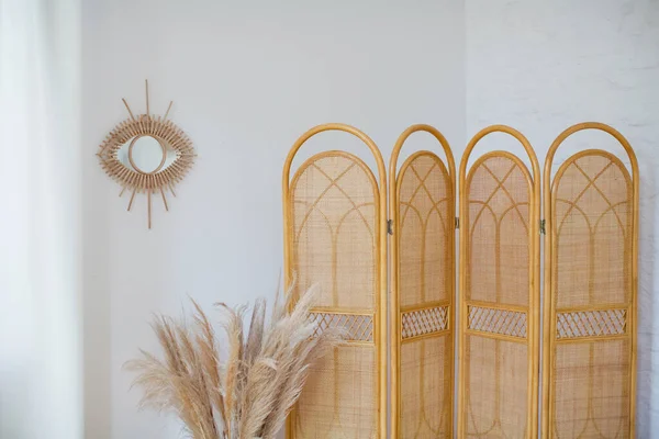 Rattan katlanır ekran ayırıcı, bir buket pampa otu ve arka planda beyaz bir ayna. Bohem iç ayrıntıları