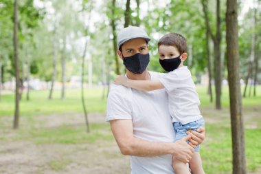 Parkta yürüyen siyah maskeli baba ve oğul. Sosyal distansing ve karantina kavramı