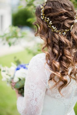 Güzel saç stili ve saçlarında altın aksesuarları olan kıvırcık gelin düğün buketi taşıyor.