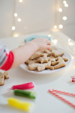 Beyaz bir tabakta renkli krema kaplı Noel kurabiyeleri. Childs 'ın eli kurabiye alır. Noel kurabiyeleri geçmişi. Fırında kurabiye, tüplerde cila, baston şekerler ve ışıklar.