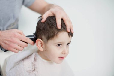 Evde karantina saç kesimi. Babası saç makasıyla saçını kesiyor. Beyaz bir arka planda yeni yürümeye başlayan oğluna.