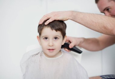 Evde karantina saç kesimi. Babası saç makasıyla saçını kesiyor. Beyaz bir arka planda yeni yürümeye başlayan oğluna.