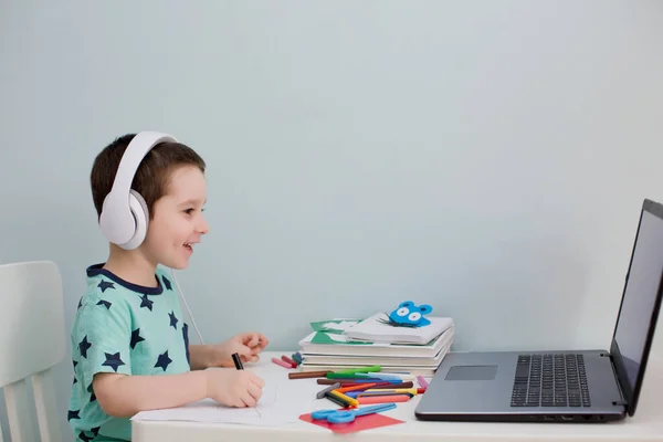 Çevrimiçi eğitim konsepti. Kulaklık takan küçük beyaz bir çocuk internette bilgisayar ve evde eğitim kavramlarıyla ilgili video çalışmaları yapıyor. Anaokulu çevrimiçi çalışması