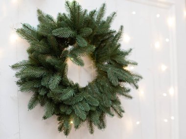 Yeşil Noel çelengi ve beyaz bir duvarda ışıklar