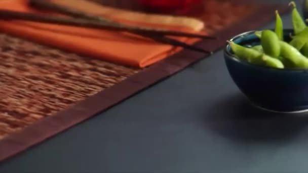 Slow pan over Asian place setting landing on chef sprinkling salt on bowl of Edamame — Stock Video