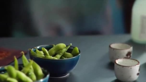 Slow pan over Asian place setting landing on chef sprinkling salt on bowl of Edamame — Stock Video