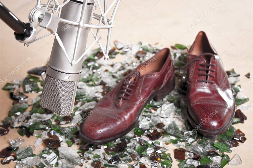 Male shoes over broken glass front a professional studio microph