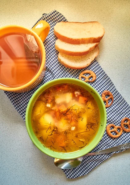 Il solito pranzo fatto in casa. Una tazza di zuppa con patate, carote e manzo. tè verde e mini-brezel. Pezzi di pane . — Foto Stock