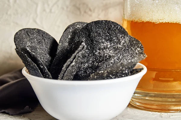 Black chips and beer. Alcoholic drink and snacks. Original beer snack. The chips with the addition of coal.