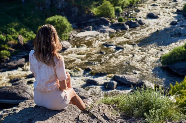 back figure woman sitting on a rock against the background of the river