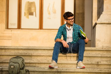 okul veya üniversite, kulaklıklar ve dizüstü bilgisayarlar ile merdivenlerde elinde duran, gülümseme ile birini bekledi gözlüklü genç öğrenci