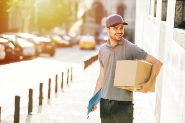 Senin nakliye işte. Onun karton kutu ve formu teslim ile ayakta, sokakta gülümseyen kap ile gri tişörtlü adam mutlu teslim