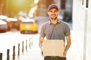 Senin nakliye işte. teslimatçı paketi, bir yerlerde sokakta teslim gülümsemeyle gidiyor kap ile gri gömlek