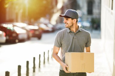 Senin nakliye işte. teslimatçı paketi, bir yerlerde sokakta teslim gülümsemeyle gidiyor kap ile gri gömlek