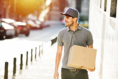 Senin nakliye işte. teslimatçı paketi, bir yerlerde sokakta teslim gülümsemeyle gidiyor kap ile gri gömlek