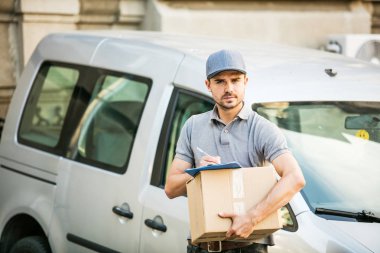 Senin nakliye işte. Onun karton ile kap ayakta ile gri tişörtlü adam genç teslimat kutusu formunu teslim, arabasının önünde sokakta istemcinin, dışarıda tanışmaya hazır için