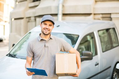 Senin nakliye işte. teslim etmek teslimatçı sokakta için doğru adres arıyor onun karton kutu ile kap ayakta ile gri gömlek