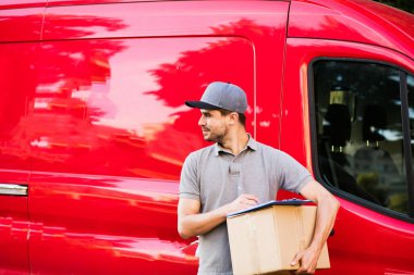 Senin nakliye işte. Onun karton ile kap ayakta ile gri tişörtlü adam genç teslimat kutusu formunu teslim, arabasının önünde sokakta istemcinin, dışarıda tanışmaya hazır için
