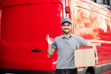 Senin nakliye işte. arabasını, paketin istemciye, dışarıda sokakta, vermeye hazır arkasında onun karton kutu ile kap ayakta ile gri tişörtlü teslimat adam güven ve ok işareti gösteren