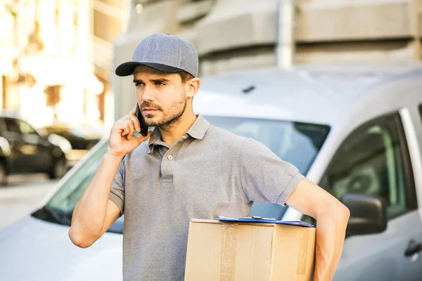 Senin nakliye işte. paketi teslim etmesi için istemci arama sokakta onun karton kutu ile kap ayakta ile gri tişörtlü teslimat adam