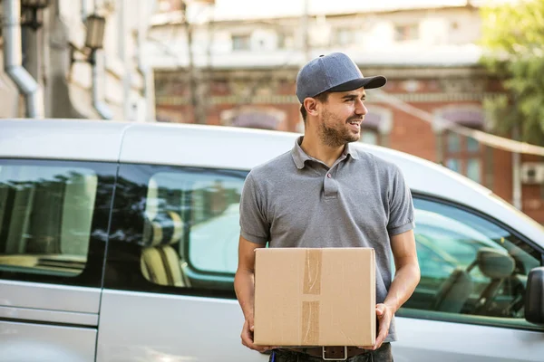 Senin nakliye işte. sokakta teslim arabasının önünde gülümseme ile kameraya bakarak onun karton kutu ile kap ayakta ile gri tişörtlü adam mutlu teslim