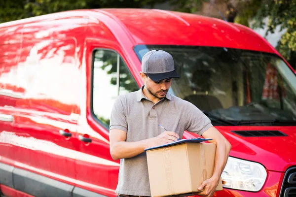 Senin nakliye işte. Onun karton ile kap ayakta ile gri tişörtlü adam genç teslimat kutusu formunu teslim, arabasının önünde sokakta istemcinin, dışarıda tanışmaya hazır için