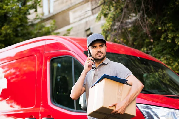 Senin nakliye işte. teslimatçı sokak paketi teslim etmesi için istemci arama ve tarafına bakarak onun karton kutu ile kap ayakta ile gri gömlek