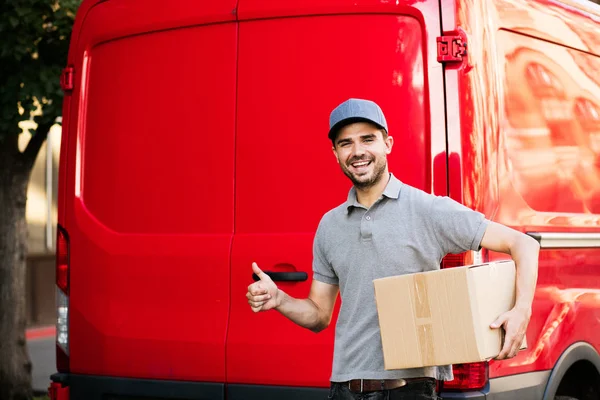 Senin nakliye işte. arabasını, paketin istemciye, dışarıda sokakta, vermeye hazır arkasında onun karton kutu ile kap ayakta ile gri tişörtlü teslimat adam güven ve ok işareti gösteren