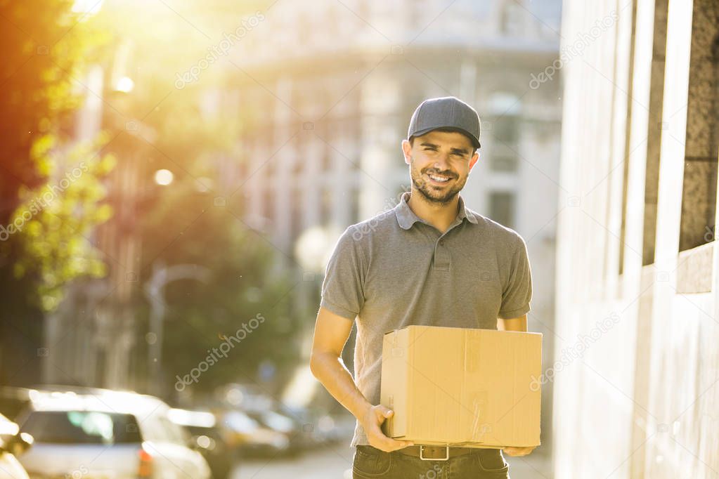 your shipping is here. delivery man in grey shirt with cap going with smile to deliver the package, somewhere on the street