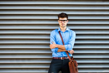 young office man waiting against a wall for something or someone, in office outfit and leather bag, standing against a wall waiting for somene with folded arms clipart