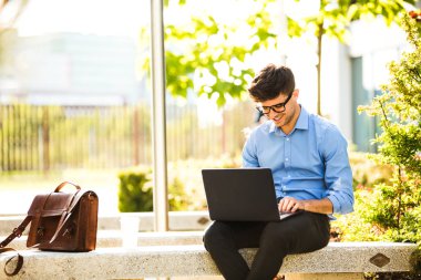 Uzaktan çalışma. Genç yakışıklı antrepreneur çalışmaktan dışında dizüstü bilgisayar, güneşli güzel gününde kutluyor