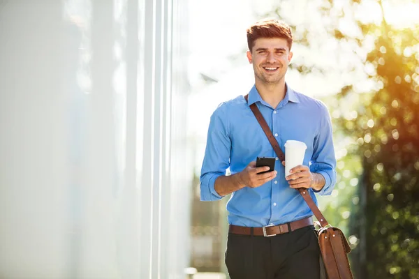 handsome young man going to work, at the office, in blue shirt with coffee in hands on a sunny day
