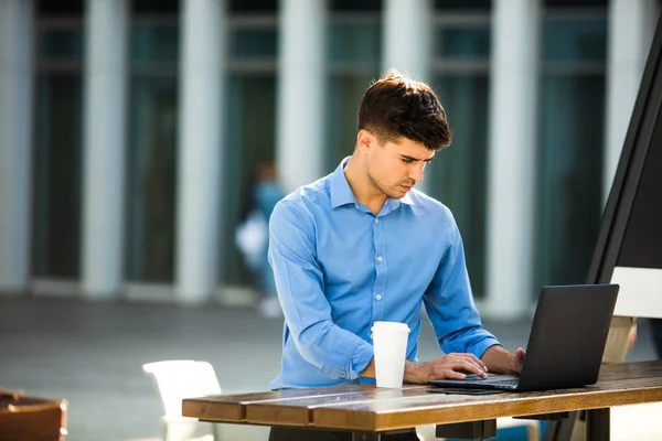 若いオフィスの人に焦点を当て 彼の隣にコーヒーを飲みながらノート パソコンで外から働いているリモート作業 — ストック写真