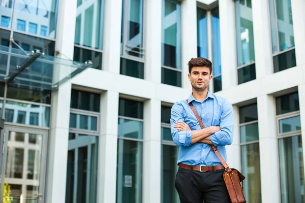 confident and successful antrepreneur, office man or corporate guy, standing with his leather bag and elegant outfit in front of an office building