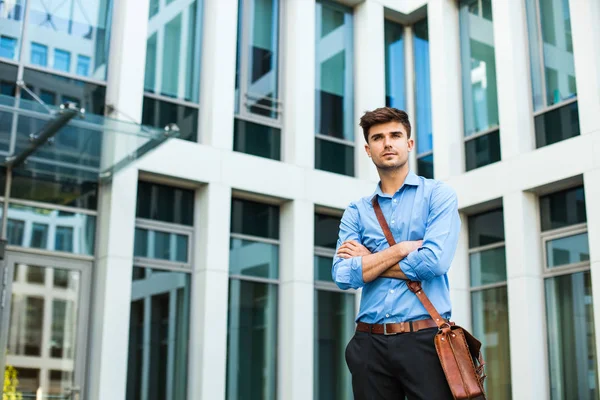 confident and successful antrepreneur, office man or corporate guy, standing with his leather bag and elegant outfit in front of an office building