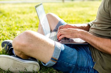 çim bir ağacına bakarak veya dizüstü bilgisayar, dışarıda park bir şehir merkezinde çalışan yalan yakışıklı genç adam, öğrenci,