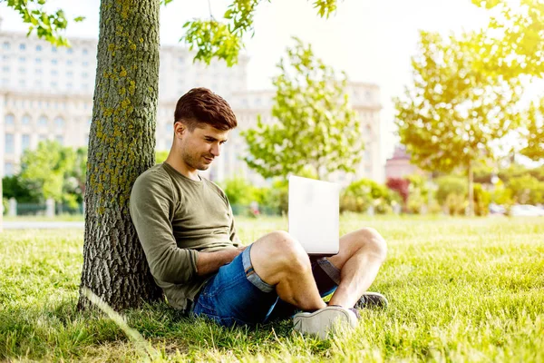Красивый Молодой Человек Студент Лежит Траве Дереве Смотрит Работает Ноутбуке — стоковое фото