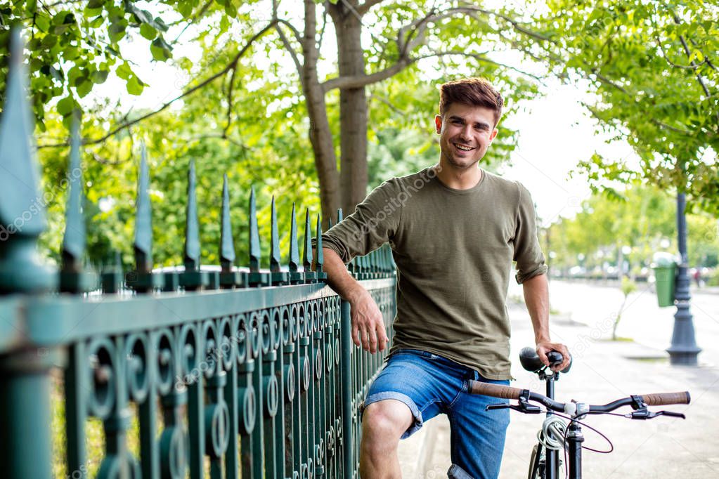handsome young man standing outside next to his bike, ready for a ride with bicyclet