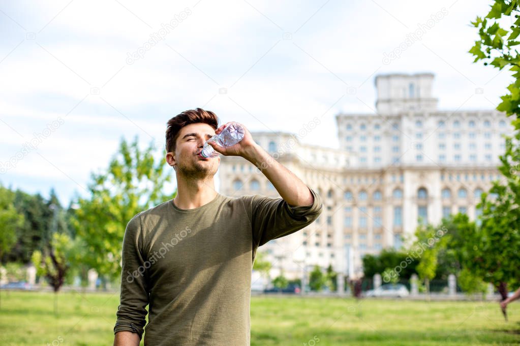 handsome young man drinking a bottle of water outside